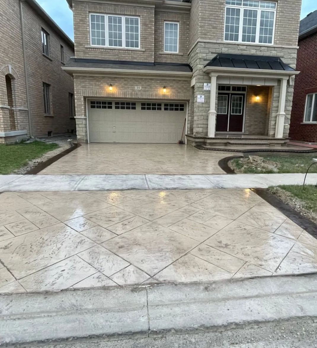 Wet stamped concrete driveway and walkway lit at dusk across a full house frontage