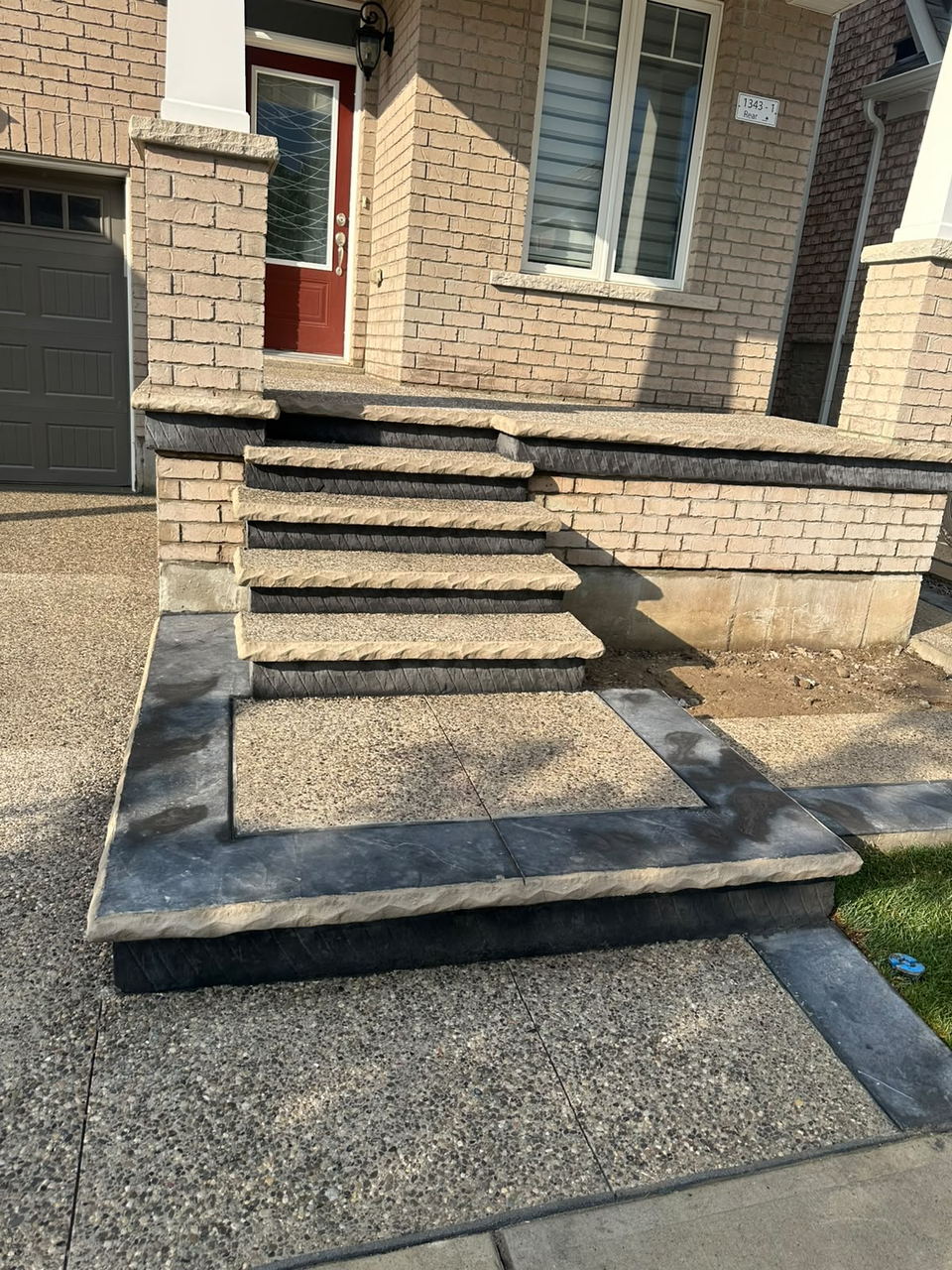 Exposed aggregate steps and landing with dark stamped borders and rock-face edging at a brick home's front entrance