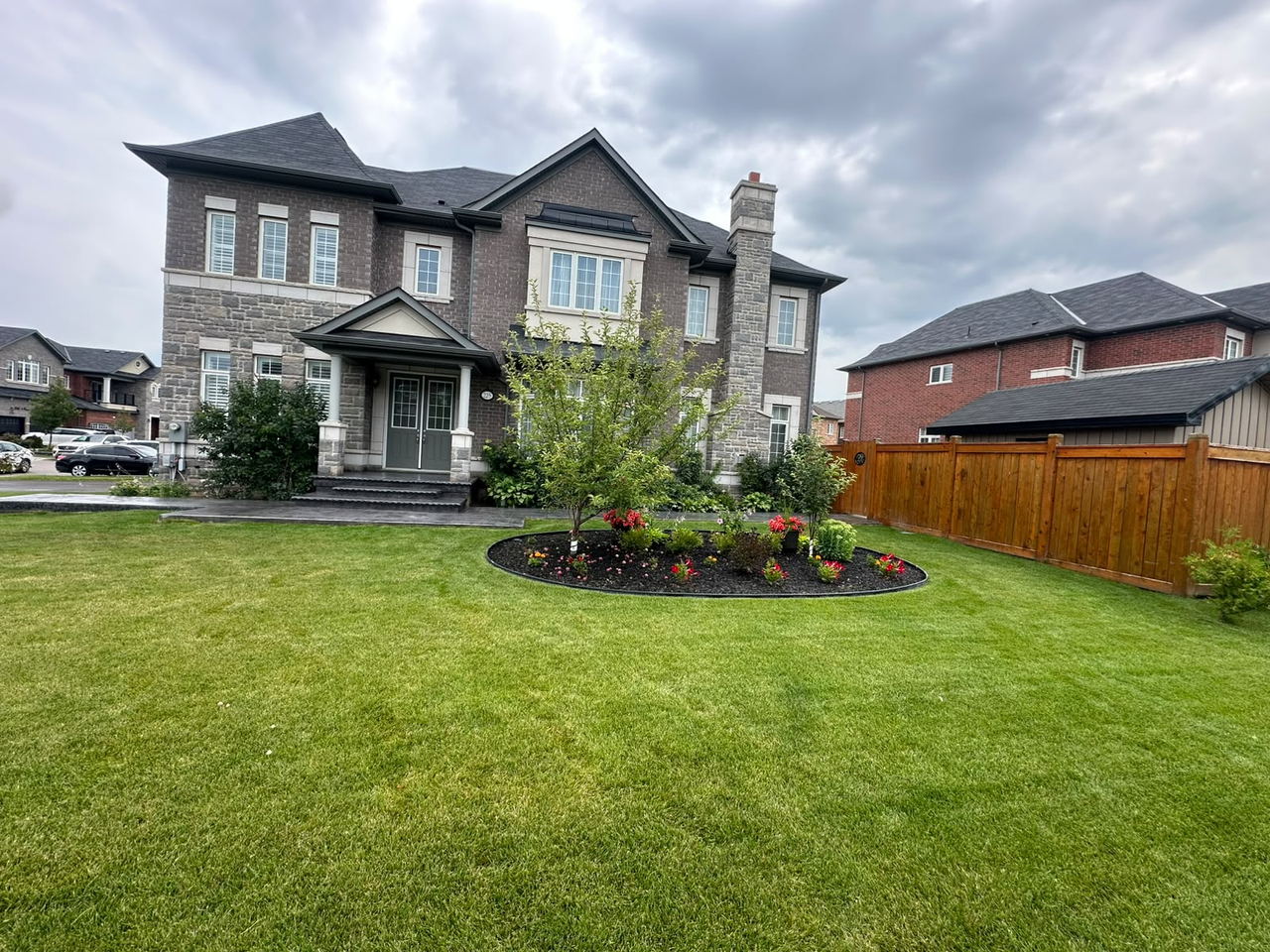 Stamped concrete walkway and entrance at a large stone home with a landscaped garden bed and new lawn