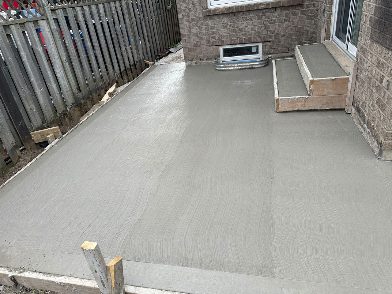 Broom-finish concrete slab poured along a side yard between the house and fence