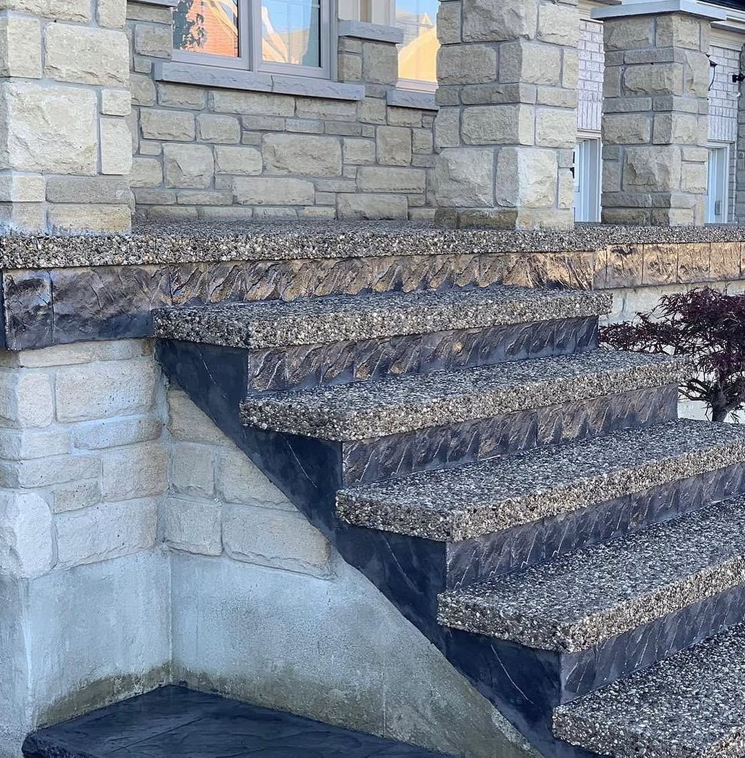 Exposed aggregate steps with dark stamped risers beside a stone-clad building in Waterloo