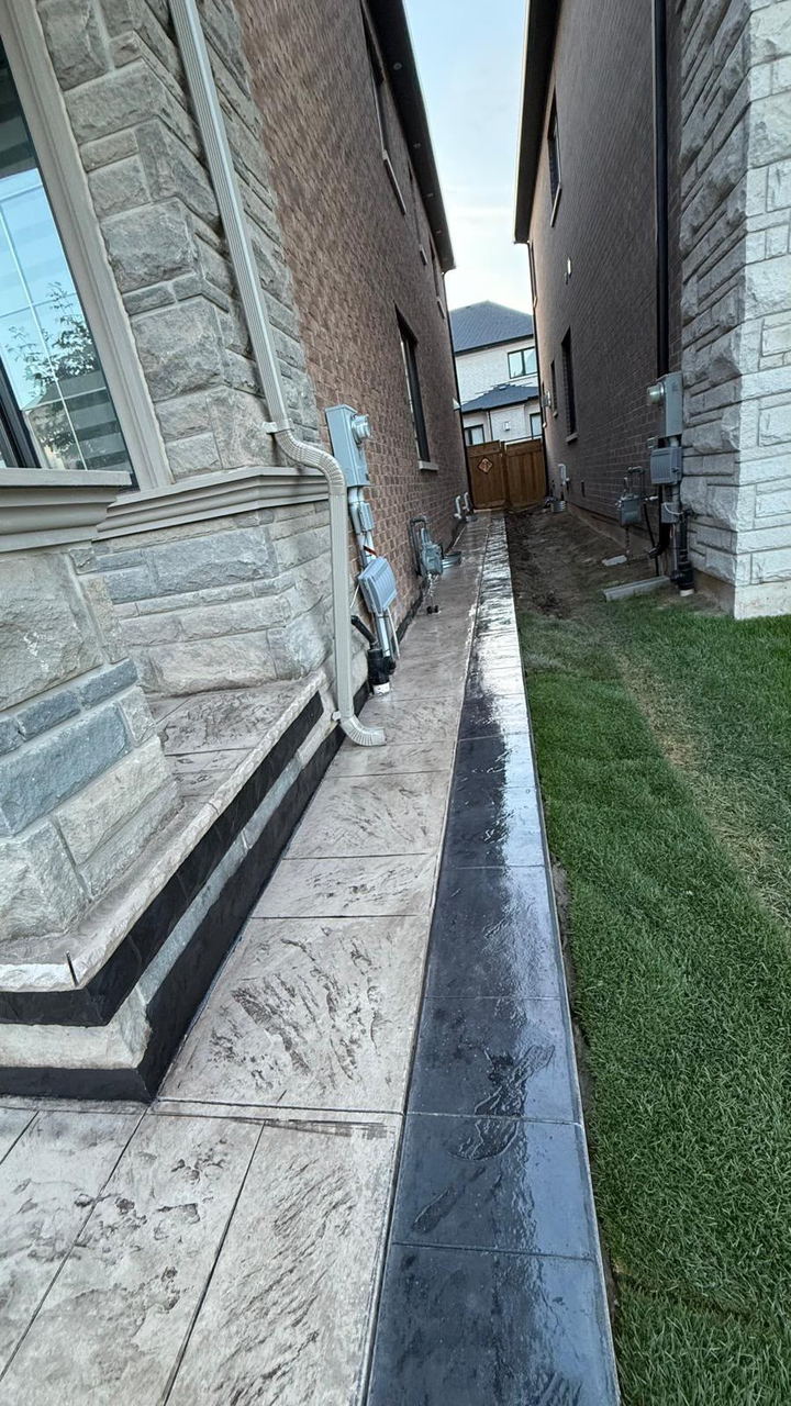 Stamped concrete side walkway with a dark border running the length of a house