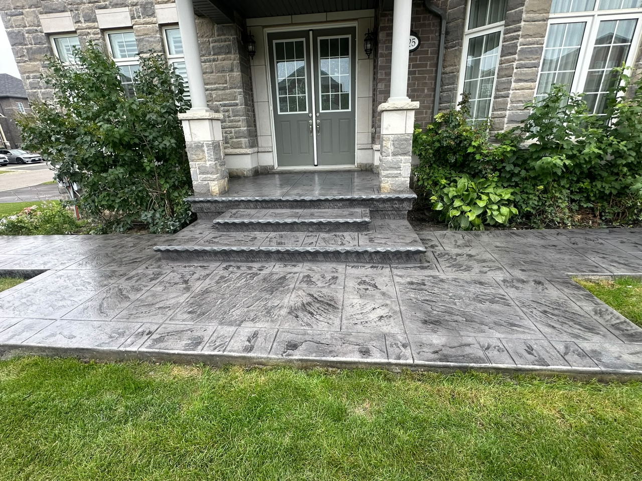 Wide grey stamped concrete walkway and steps running along the front of a stone house